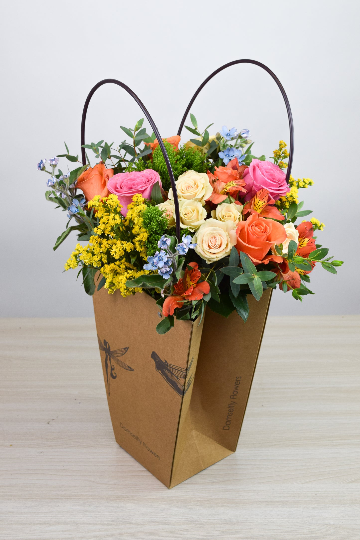 Colorful floral bouquet in a ecofriendly carrier bag placed on a wood surface with a neutral background