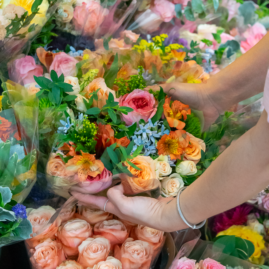 Person holding a colorful bouquet of flowers amongst a variety of bouquets in a market setting