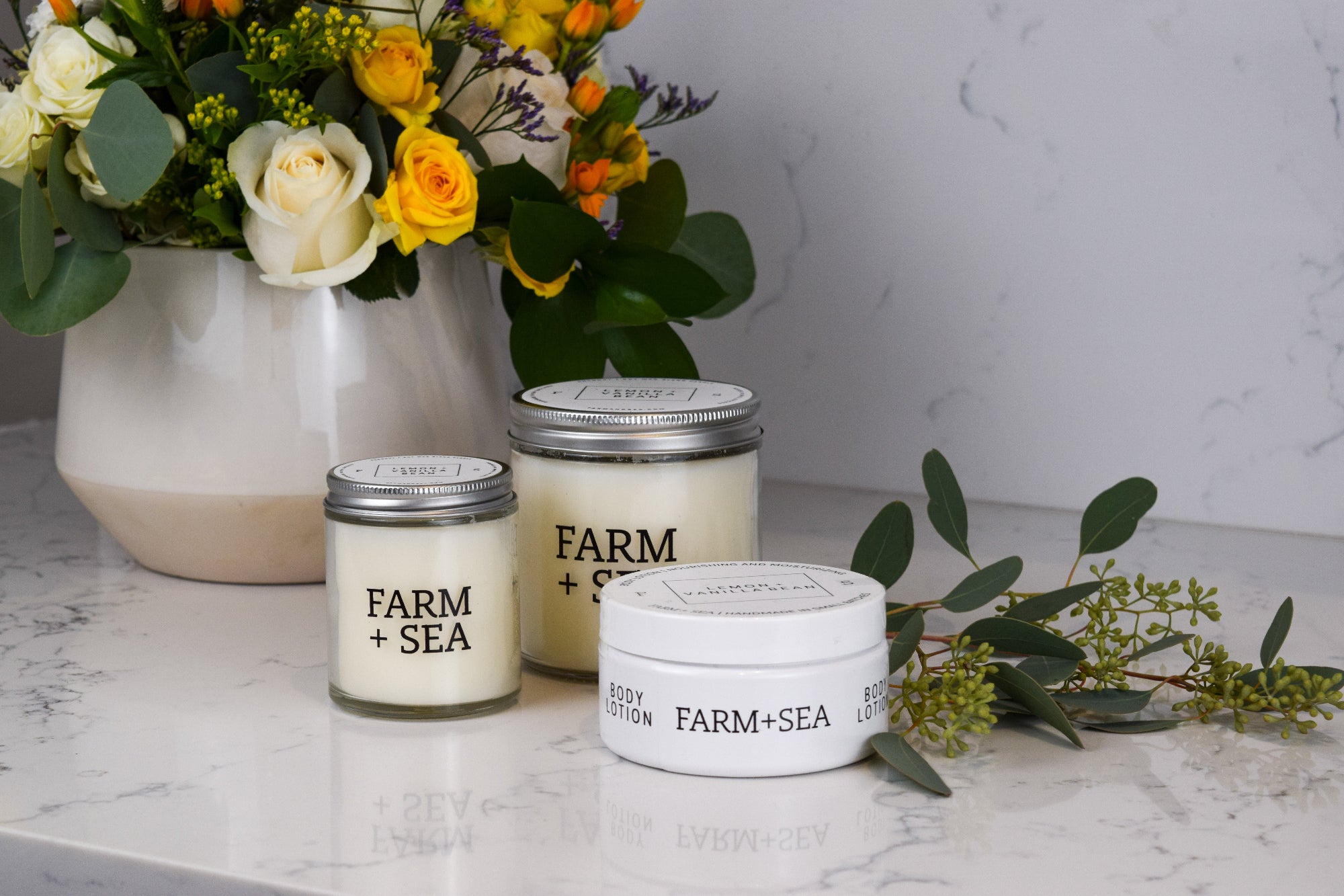 Three 'Farm + Sea' products on a marble surface with flowers in the background